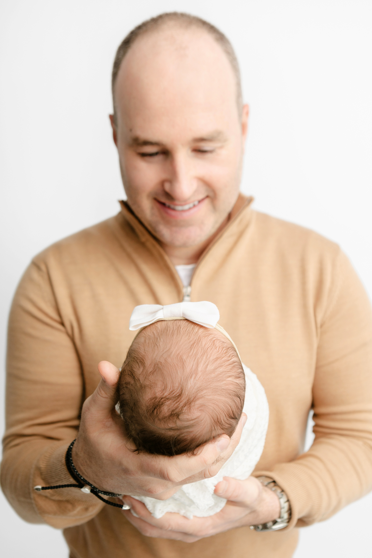 new father holding his baby girl in his hands and smiling down at her; studio newborn photography