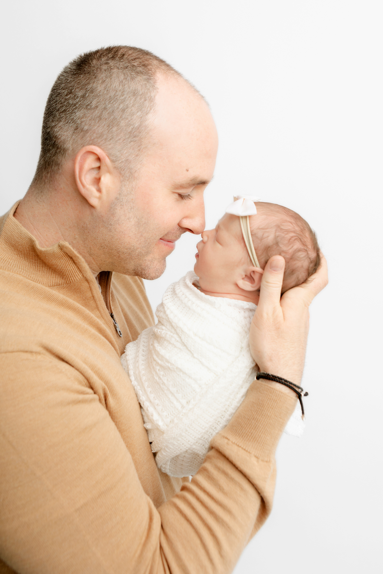 new dad with very short hair and stubble touching noses with his newborn baby girl