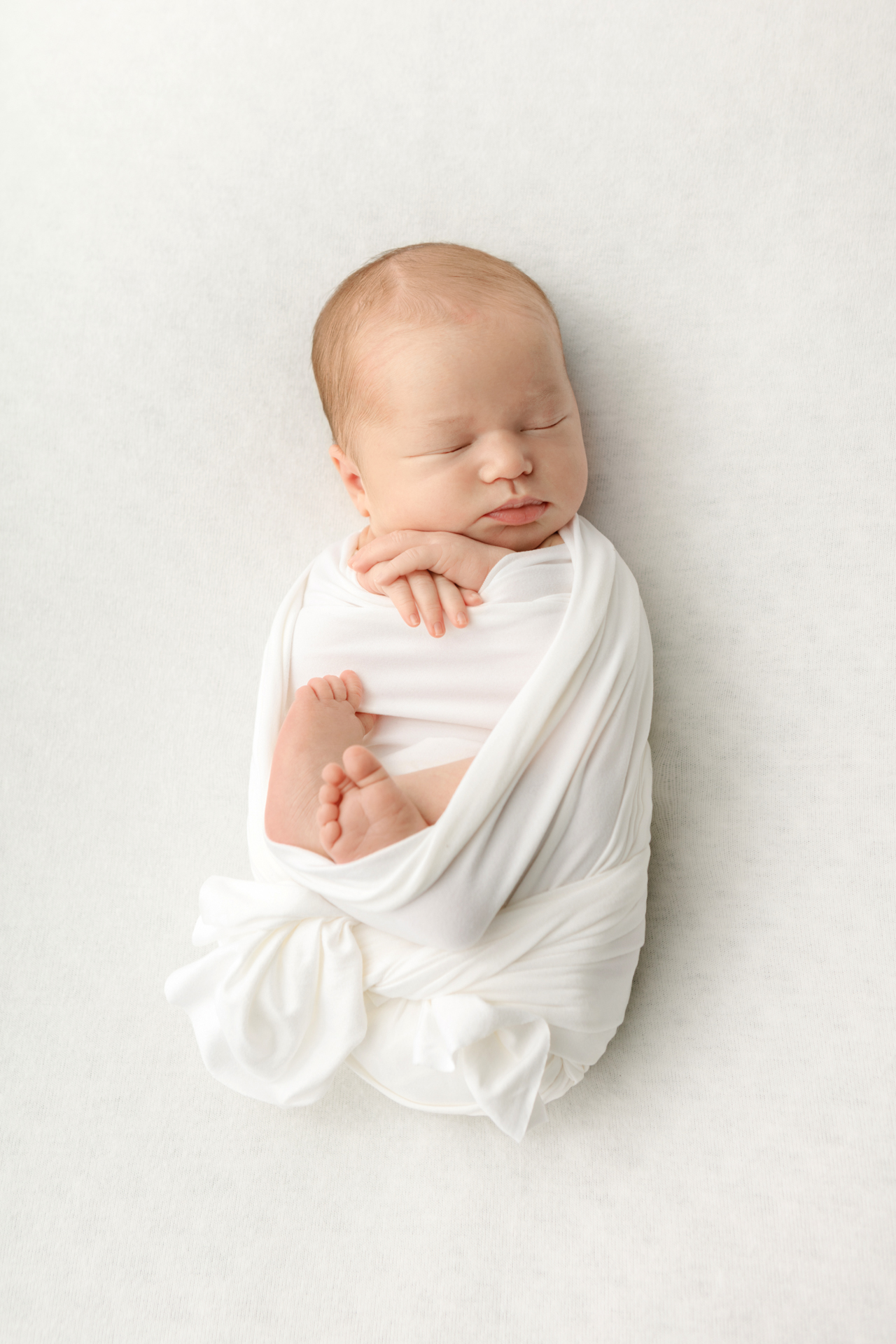 newborn baby girl swaddled in a stretchy white swaddle tied with a loose knot