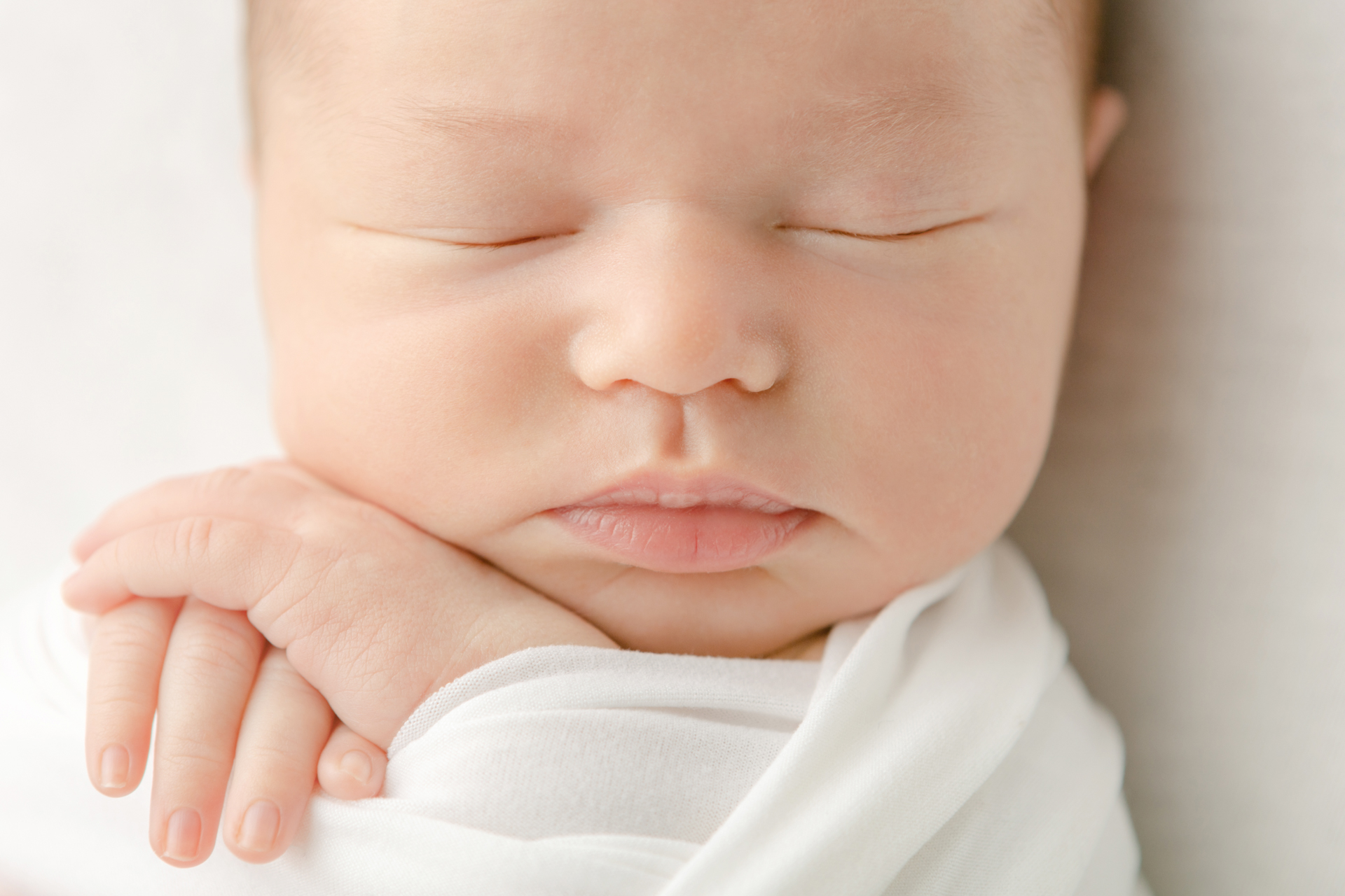 close-up photo of a sleeping newborn baby girl with her hands folded under her chin