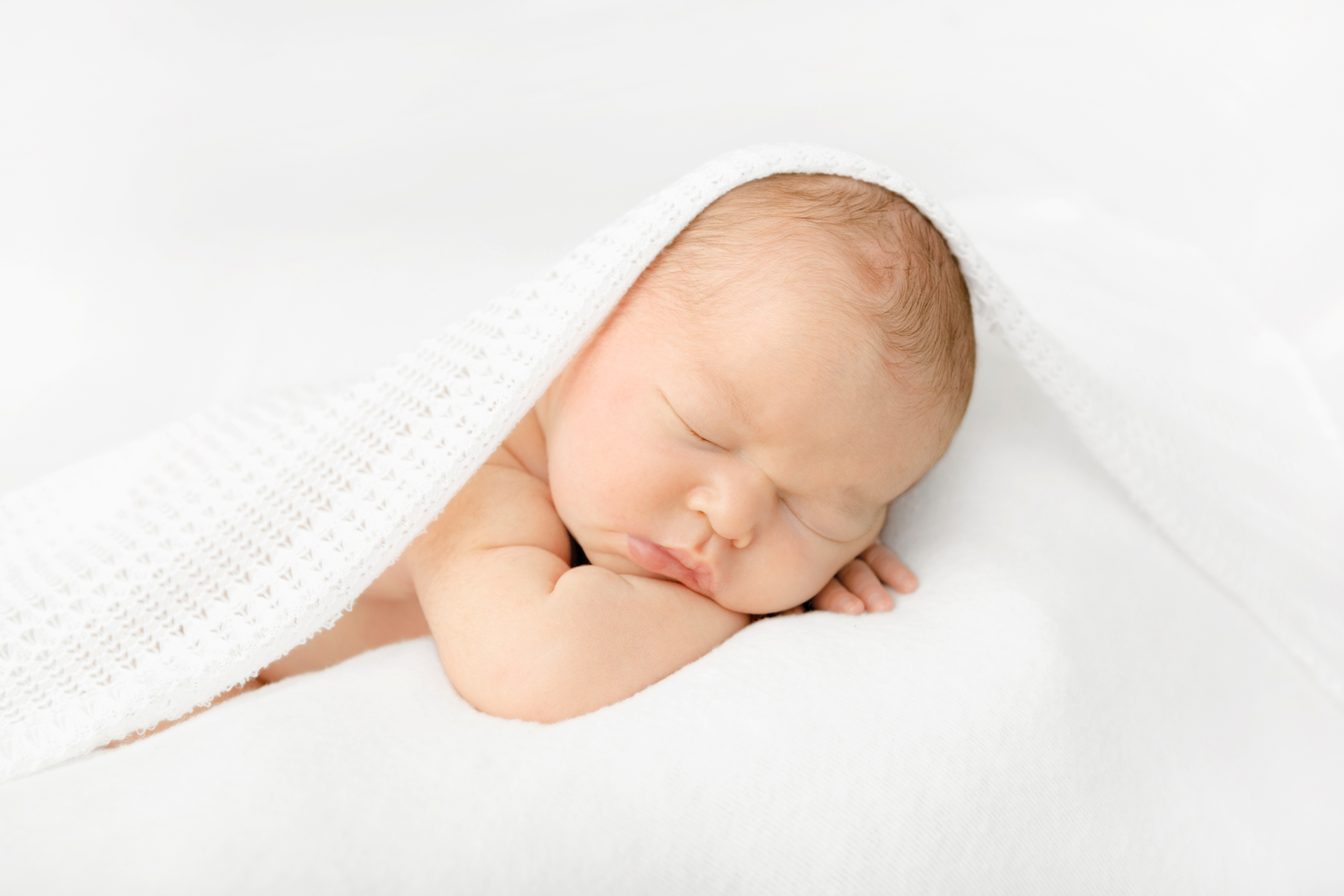 chubby newborn baby girl with her hands folded underneath her cheek as she sleeps