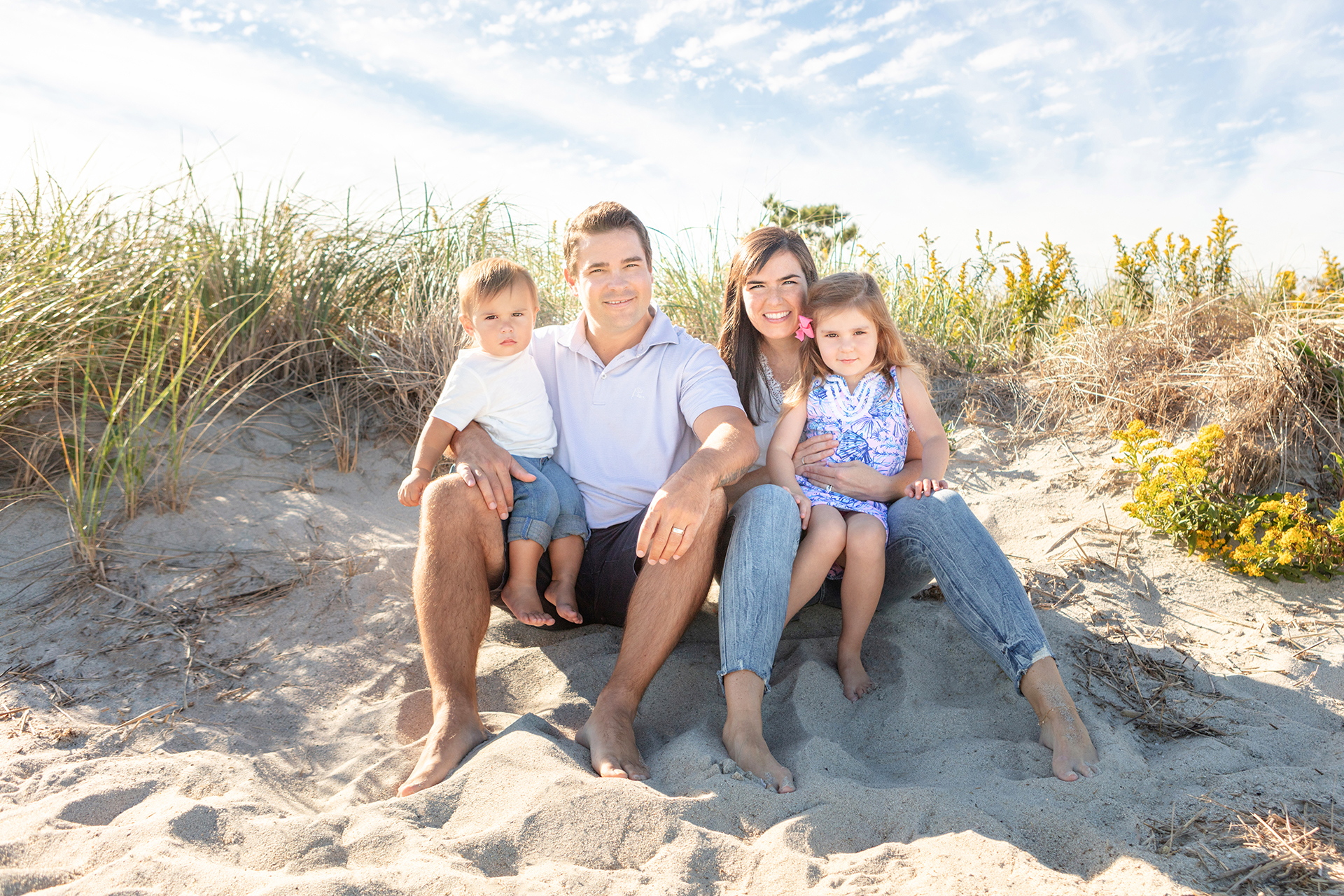 family of four sitting in the sand and grass on a Connecticut beach