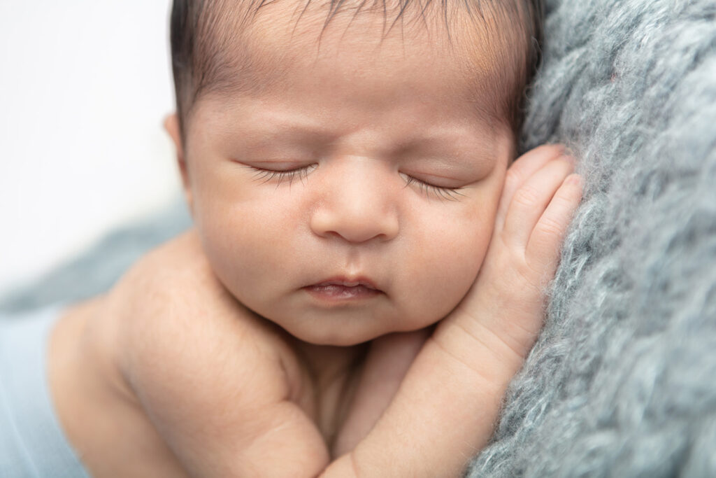 Newborn baby boy Noah appears to be sleeping on a stormcloud as he lies his head on his hand, resting on a gray-blue alpaca blanket with a chunky, wide weave.