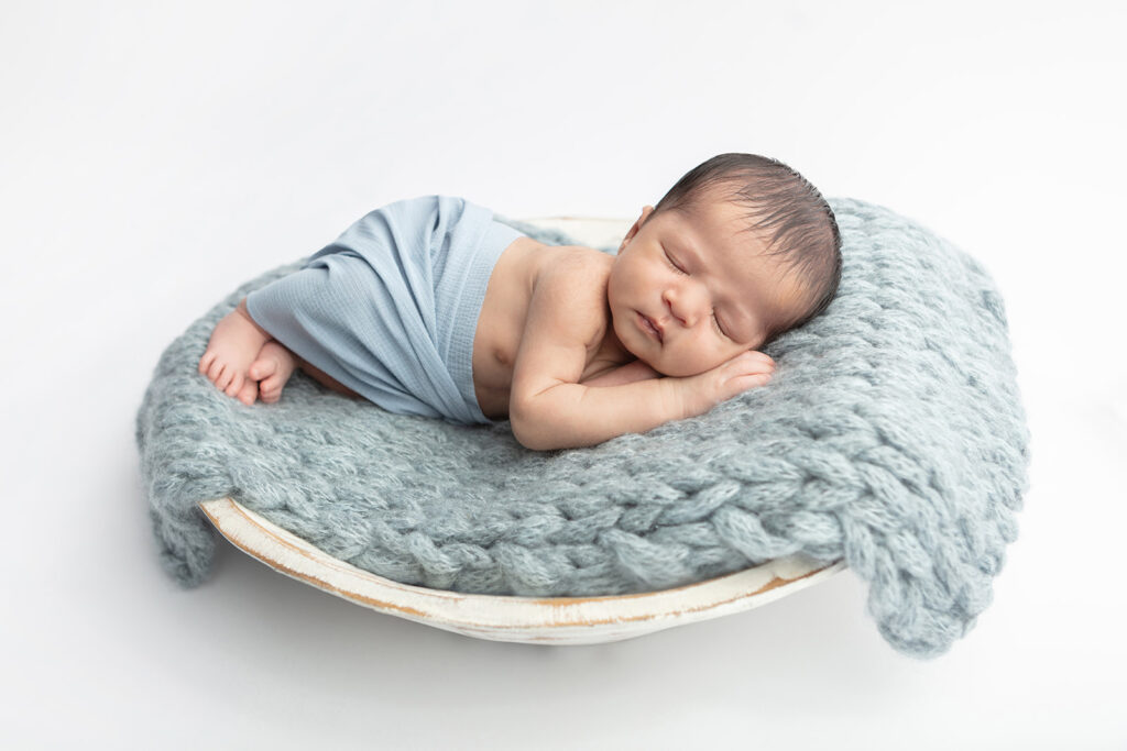 The perfect rustic modern farmhouse newborn portrait. Newborn baby boy Noah, lightly draped in a dusty blue muslin swaddle, sleeps peacefully in a shabby chic, oversized wash bowl lined with a chunky knit, dusty blue blanket woven from alpaca hair.