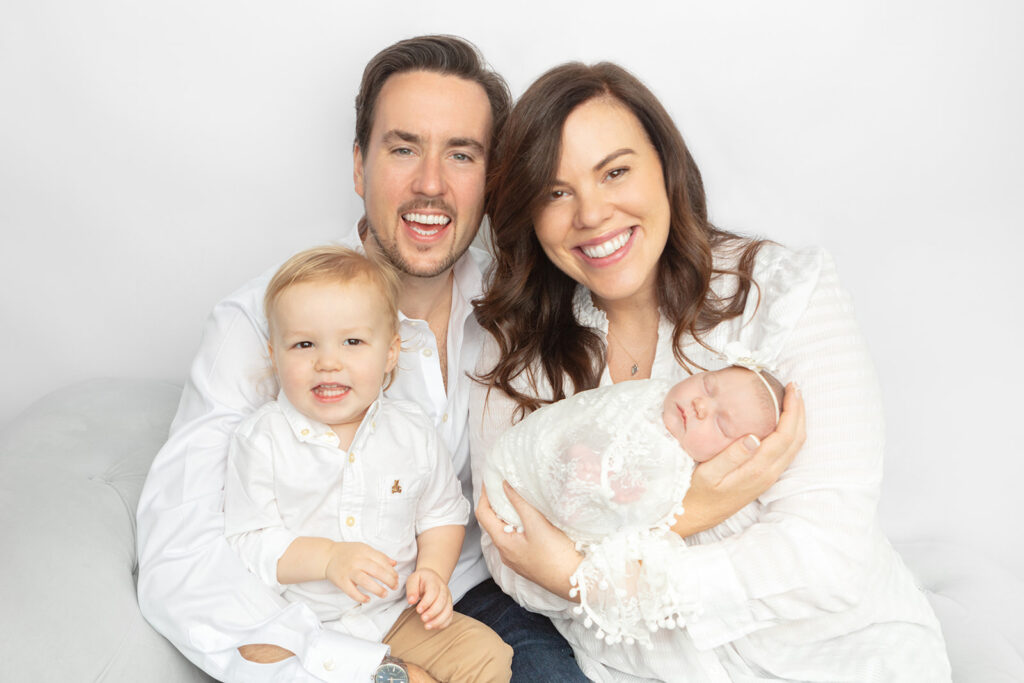 A newly minted family of four are photographed smiling and laughing (all except the newborn baby girl, who sleeps away), in the Looking Up Photography studio in Greenwich, Connecticut.