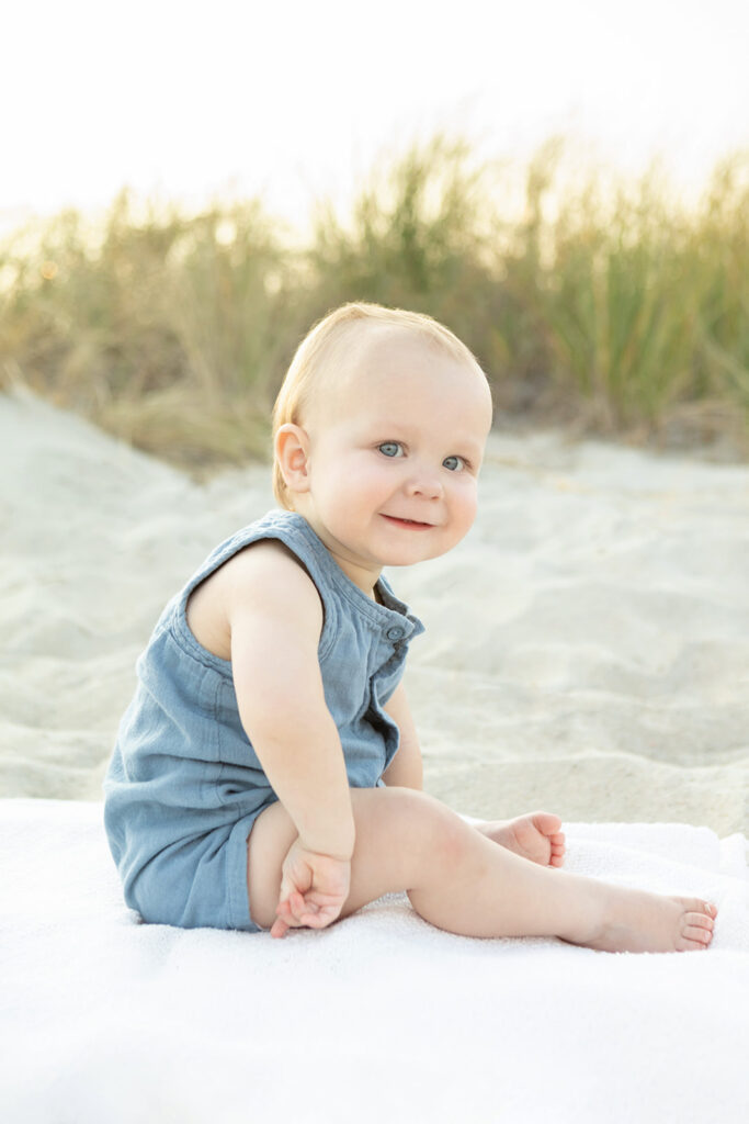 Beach portrait of an adorable tyke named Logan, who smiles mischievously at the camera with his dimpled smile and big blue eyes, his right hand turned outward playfully.