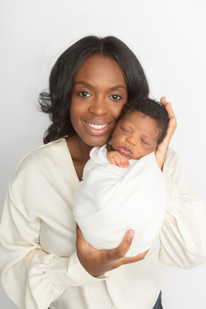 Black mom and newborn son. A beautiful, smiling mom, proudly displays her newborn son for the camera. She holds her swaddled son in her hands, touching cheek to cheek.