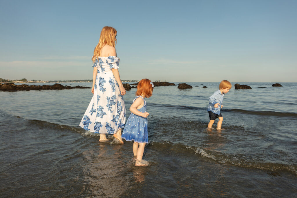 A red-headed trio (a mama and her two young children) are bathed in Golden Hour lighting as they walk and splash in the water along the Connecticut coast.