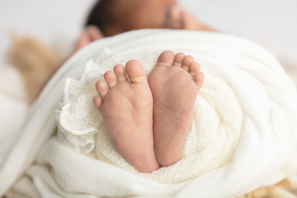 Squishy little baby toes and feet. Is there anything better? Baby feet peek out from a lightly woven blanket and a thicker swaddling blanket, both in a cream color.