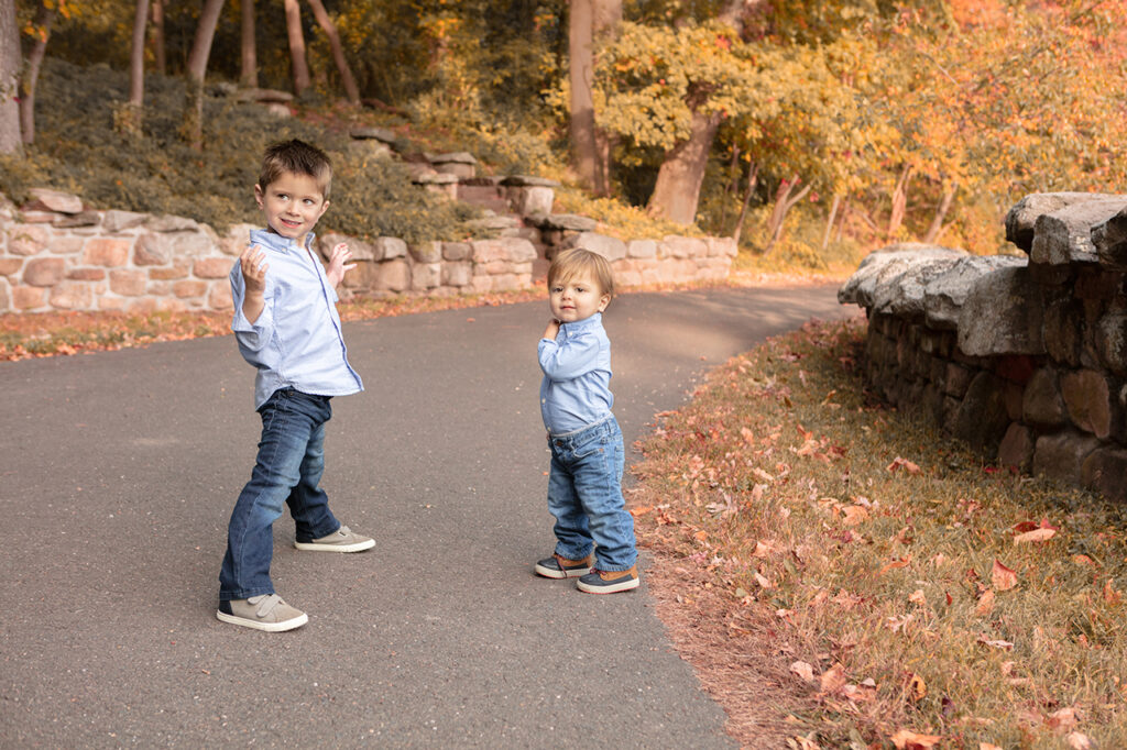 Young brothers in a fall portrait, laughing and playing amidst the vibrant autumn leaves, showcasing their strong bond and carefree spirit. Photographed by Karen Kahn