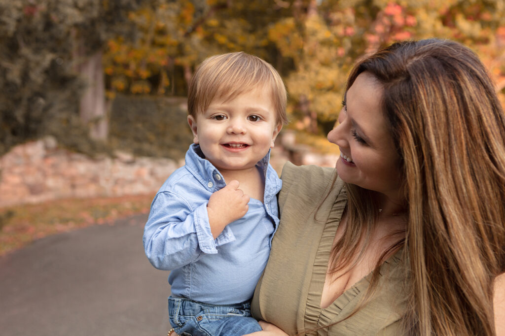Mother and son embracing in a beautiful autumn portrait, surrounded by colorful foliage and sharing a heartwarming moment together. The little boy smiles at the camera as mom smiles at him.