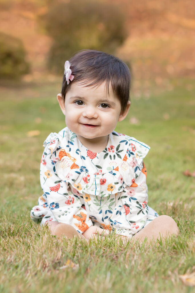 A darling little girl is photographed wearing a fall printed dress with a large, ruffled collar. She wears a barrette in her hair and smiles sweetly at the camera.