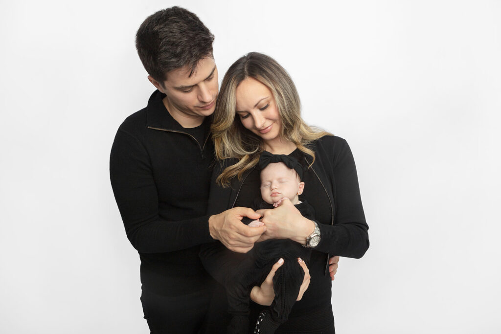 Dad, mom, and newborn baby girl all dressed in black, photographed classically in the Looking Up Photography Studio, Greenwich, Connecticut.