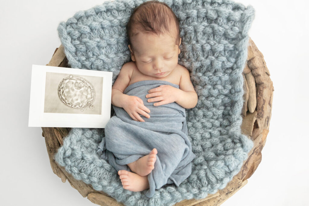 Newborn baby Matteo is photographed lying relaxed in a driftwood basket lined with a chunky knit blue square. Next to him is the very first photo of him in his mom's womb.