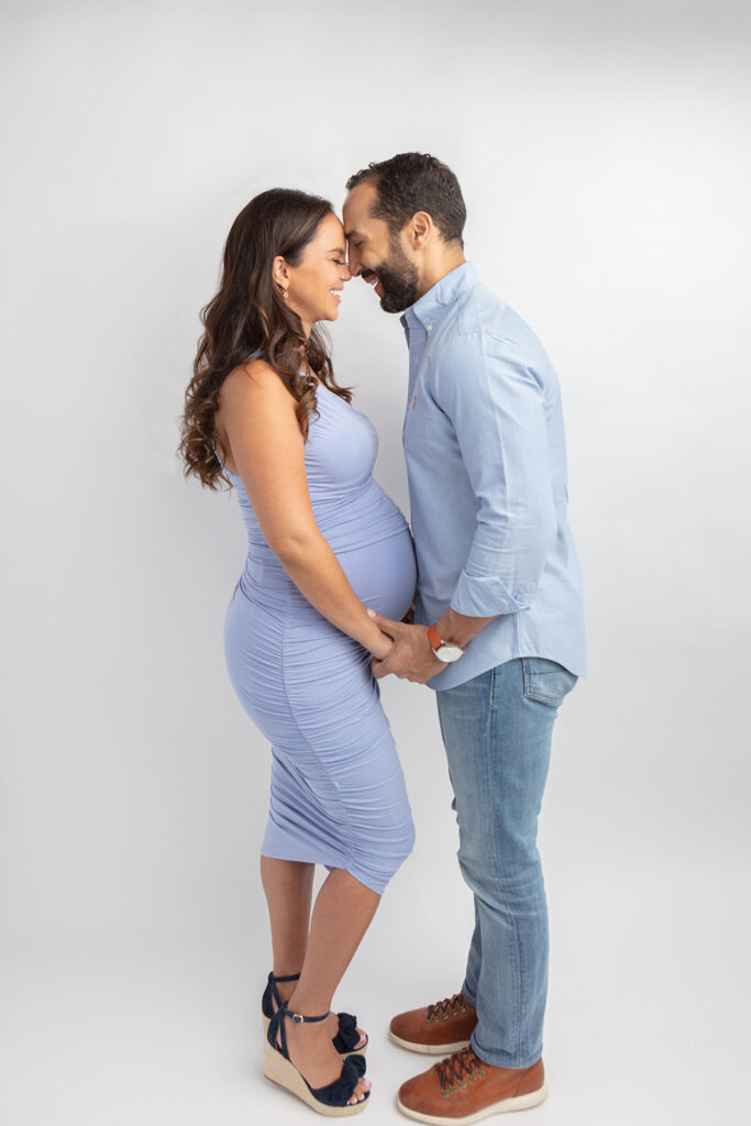 In a couples maternity portrait that looks straight out of an ad campaign, a beautiful multicultural couple touch noses, laughing and holding hands