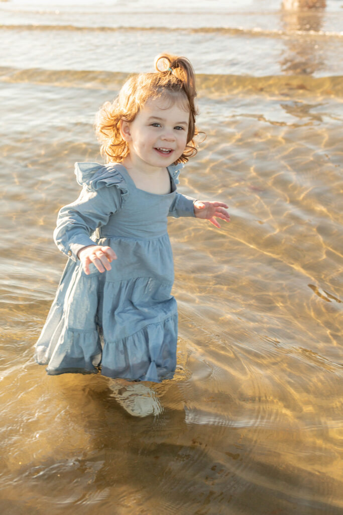 Two and a half year old Blake wades into the Atlantic ocean in her white mary jane style shoes, the hem of her dress soaked, and a smile on her toddler face.