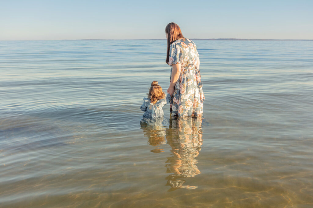 A mother and daughter wade into the clear blue Atlantic ocean at sunset, the horizon hardly discernable from the waterline in an ethereal portrait captured by Karen Kahn