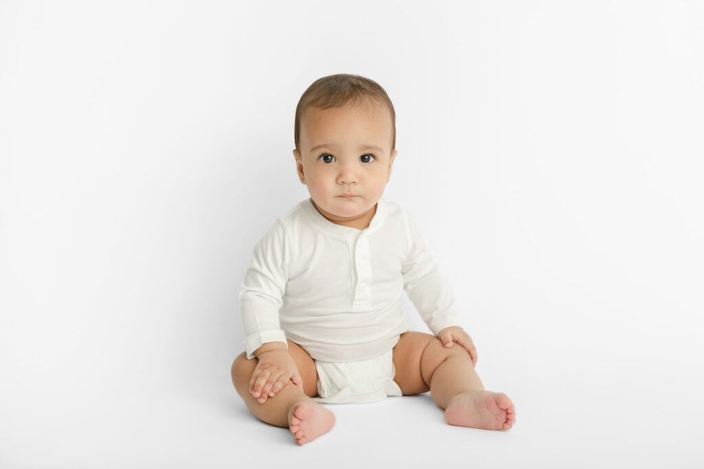 Baby Ezra is photographed with a more serious expression on his face, sitting up in the Looking Up Photography studio in Greenwich, Connecticut
