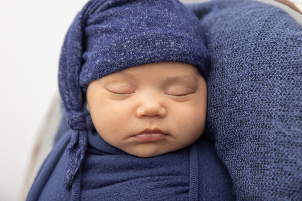 A classic newborn baby portrait of baby Mateo, photographed in a heathered navy stocking cap, navy swaddle, on a blue blanket in the Looking Up Photography studio