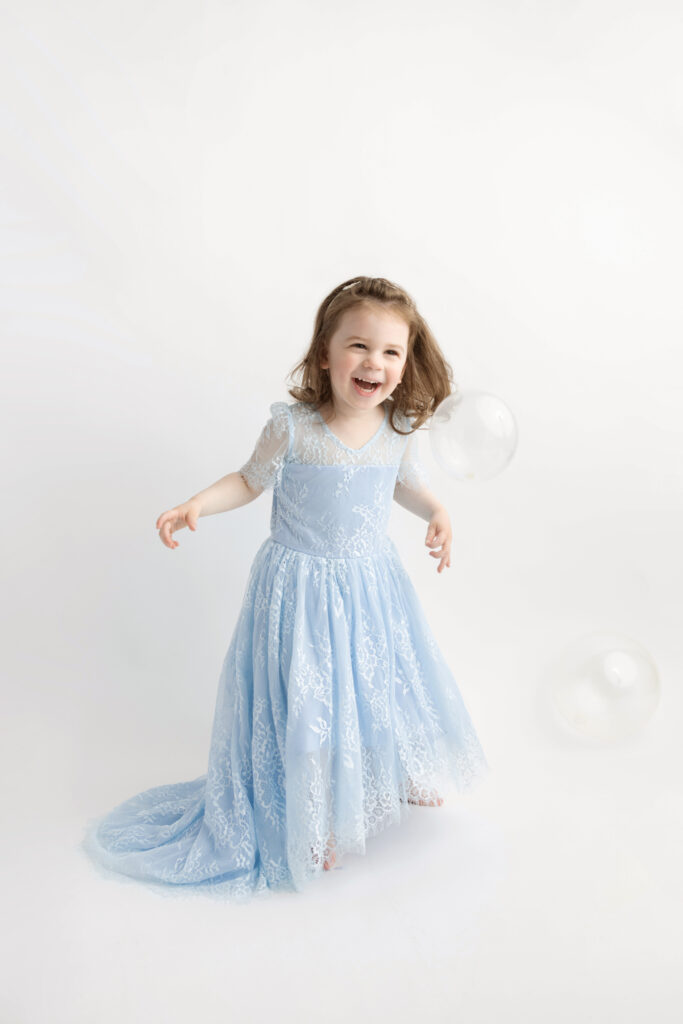 three year-old Blake dances around the Looking Up Photography studio in the Cos Cob neighborhood of Greenwich, Connecticut; she wears a lacy, light blue dress that's very Cinderella-esque