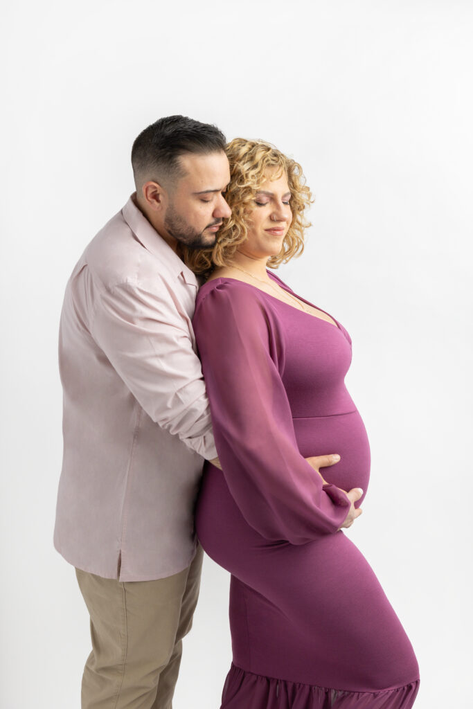 Couples maternity session inspiration; couples maternity portrait inspiration. Charles stands behind Courtney, cradling her pregnant belly, in a modern maternity portrait.