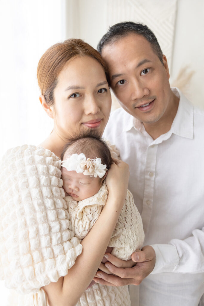 new parents Grace and Joseph pose with their newborn daughter, Chloe; the trio are all styled in shades of white and ivory, and are photographed in their home by Karen Kahn
