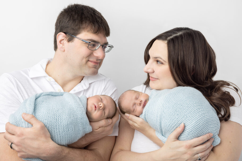 Newborn twin boy photo inspiration. New twin parents Patrick and Leah look at each other with love and amusement in their eyes, as each of them holds one of their newborn twin boys.