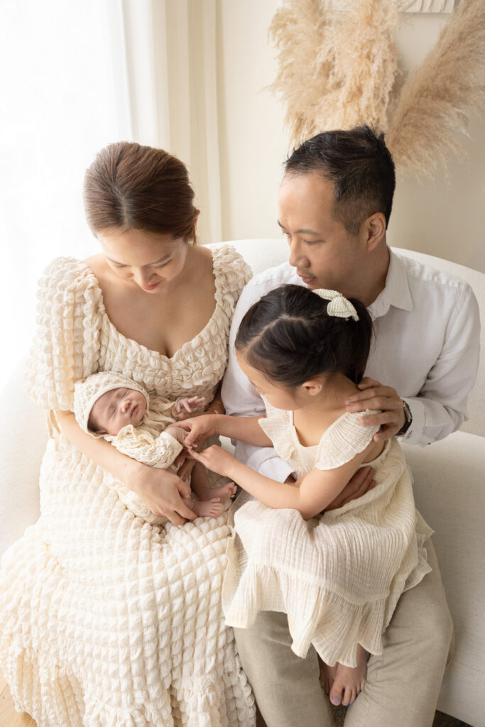 a beautiful family of four, photographed in neutral textures of gauze and linen, sit in their northeastern home, exemplifying the modern-contemporary family