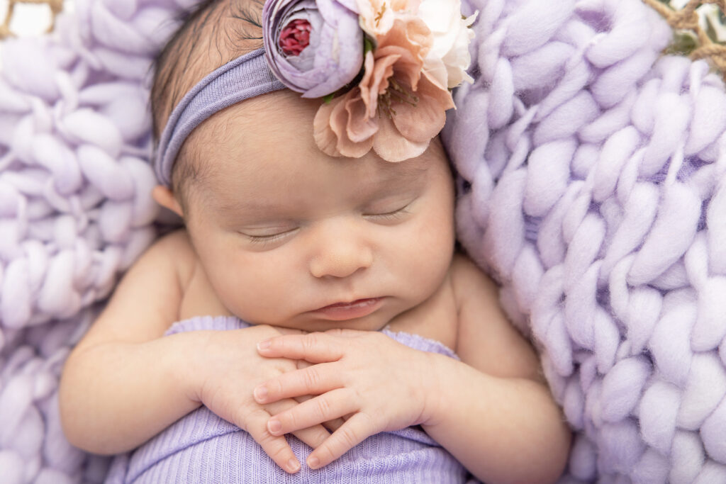 A closeup image of a premature newborn baby girl named Fallon. Fallon wears a faux floral headband with dusty pink flowers and lilac colored ranunculus.