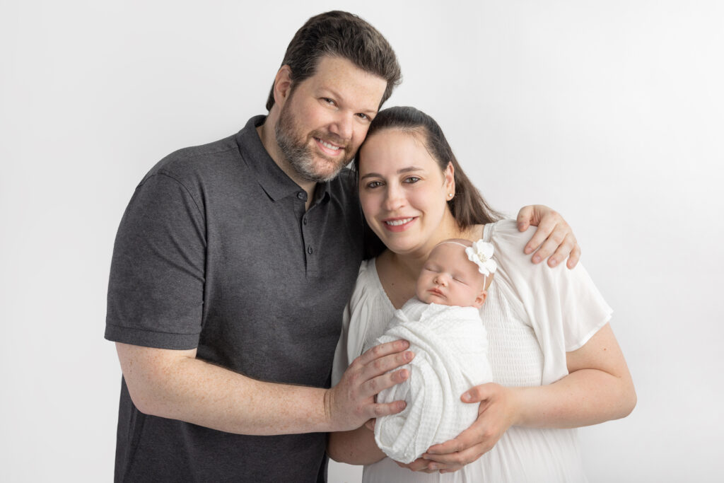 New parents are happily photographed in the Looking Up Photography studio in Cos Cob, Greenwich, Connecticut. The duo hold their newborn baby girl in their hands.