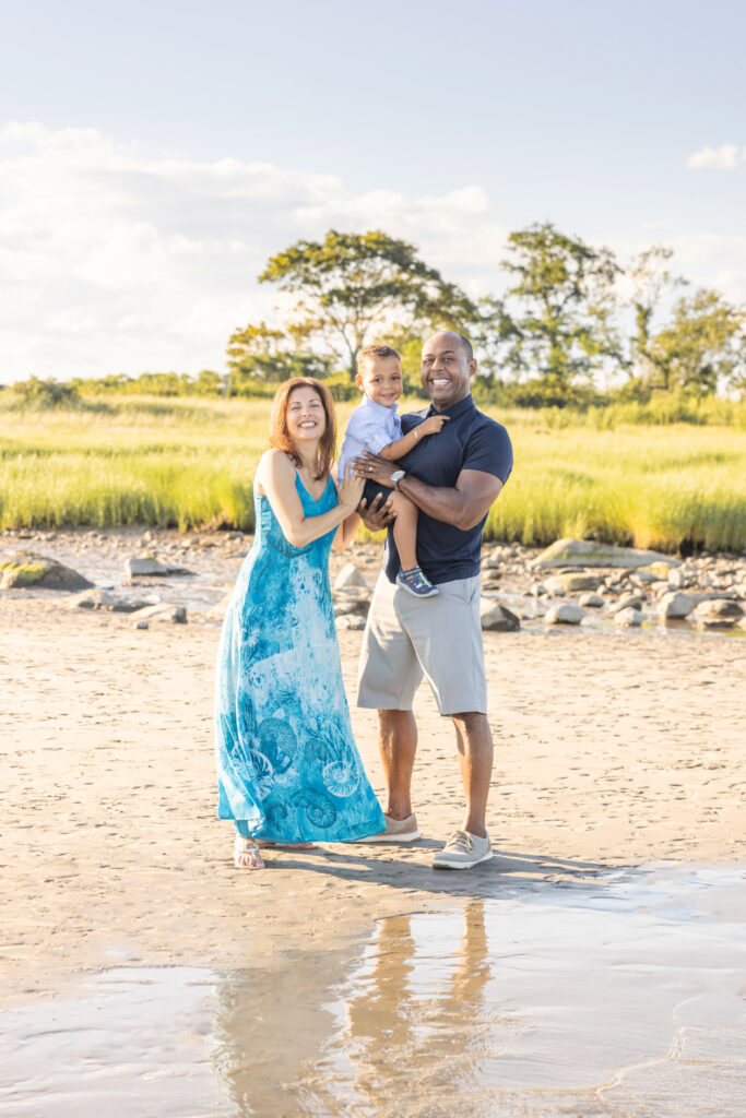 A multicultural family of three are radiantly photographed by Karen Kahn, of Looking Up Photography, on the Connecticut coastline during the golden hour.
