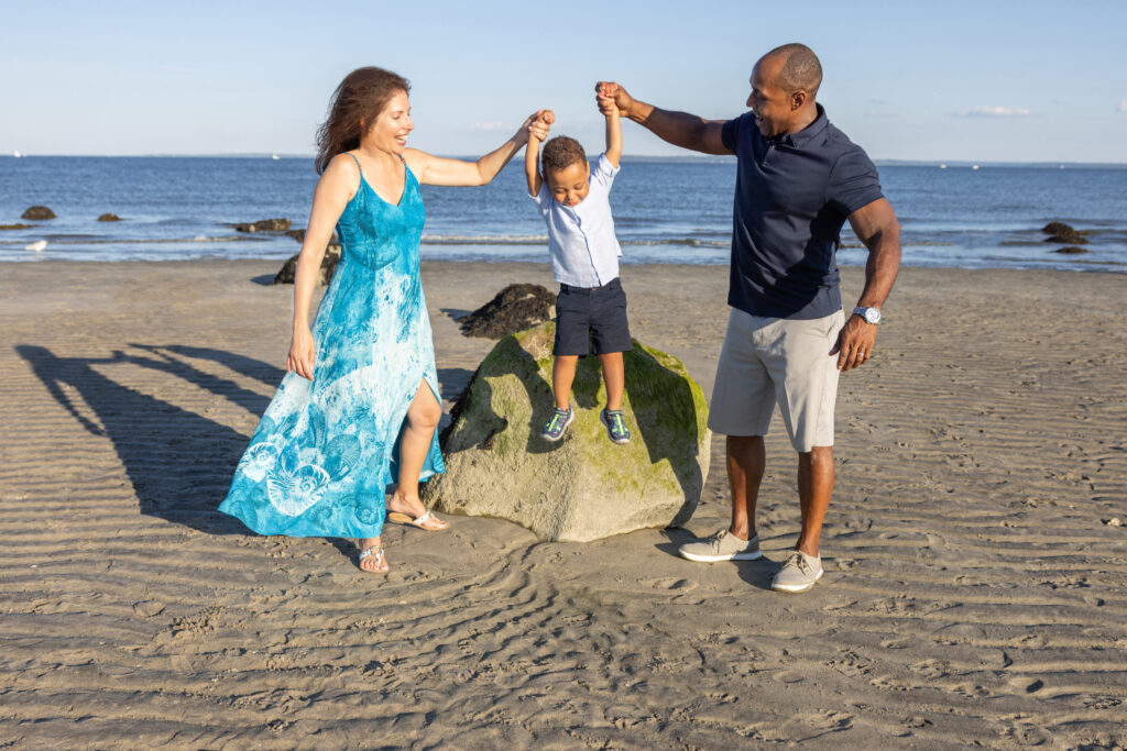 A multicultural family of three are photographed during the golden hour, along a Connecticut beach. Their long shadows dance playfully behind them, as the waves lap gently onto the sand.
